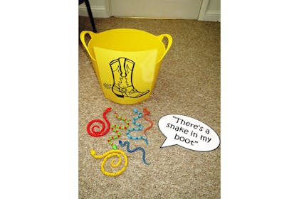 Yellow bucket with a boot drawn on it next to toy plastic snakes and a sign saying 