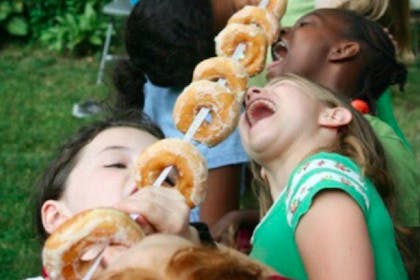 Children eating doughnuts from a pole