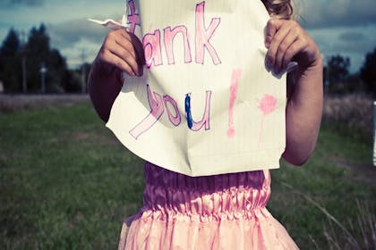 girl in field holding paper with thank you written on it
