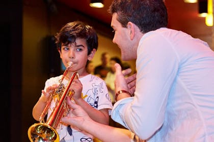A young boy tries playing the trumpet while an adult helps