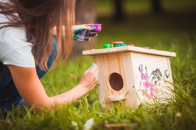 Young girl painting a wooden bird house in the garden