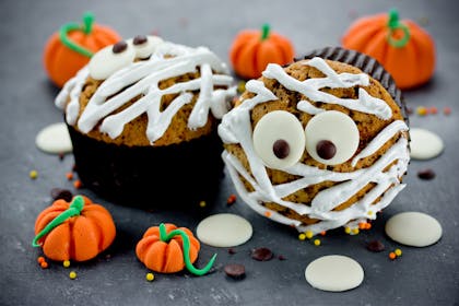 Halloween mummy cupcakes decorated in white icing with pumpkin sweets scattered about
