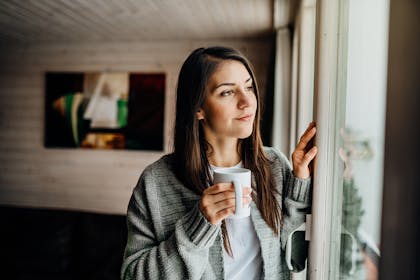 woman looking out of window holding a cup of coffee