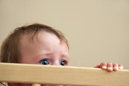 Scared baby looking over rim of crib