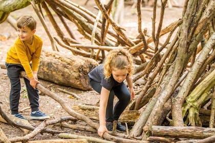 A young boy and girl lift large sticks to create a den at Anglesey Abbey | © National Trust Images / Antonia Gray