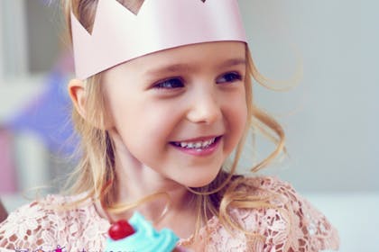 girl with paper crown eating cup cake