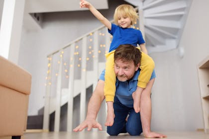 A dad crawls on the floor while giving son piggyback round the house