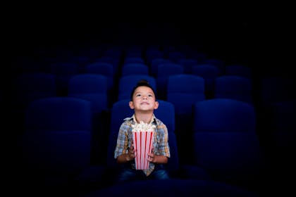little boy sitting in cinema holding tub of popcorn