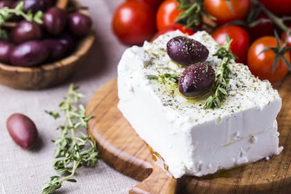 block of feta cheese topped with olives on chopping  board