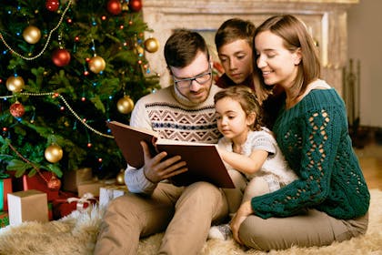 Family reading a book together in front of the Christmas tree