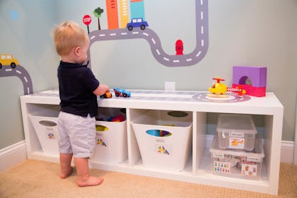 Boy toddler playing with toy cars on a low Ikea storage unit