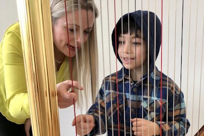 A woman and a young boy in a hoodie examine the strings of a harp