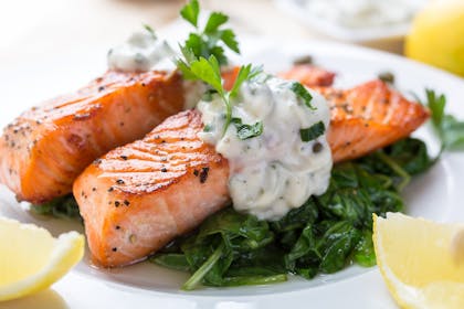 Grilled salmon with tartar sauce, spinach and lemon wedges.