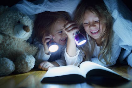 Kids reading under bed covers with a torch