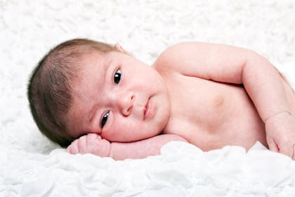 Newborn baby with a full head of hair lying on their side for photoshoot
