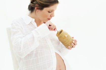 pregnant woman in while eating peanut butter from jar