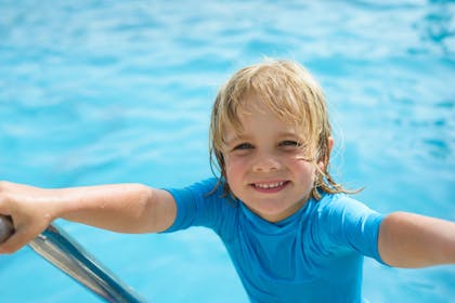 Blond haired boy climbing up the steps of swimming pool