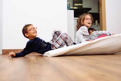 Two kids sit on a duvet for blanket sledding around the house