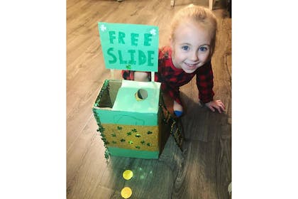 Kid sits next to leprechaun trap made from a green cardboard box and sign that says 