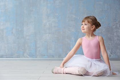 Girl dressed as ballerina in pink leotard, white tutu and ankle warmers