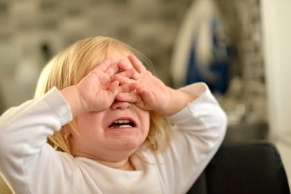 Toddler crying and covering their eyes with their hands
