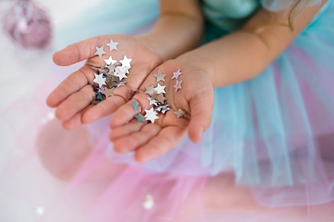 Kid in blue and pink tutu holding silver star sequins in hands