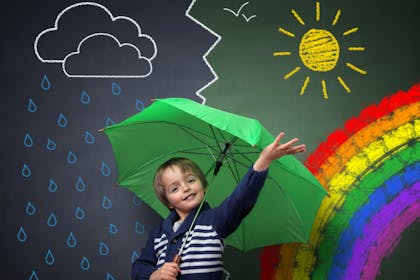 boy with green umbrella standing in front of chalkboard with different weather images drawn on it