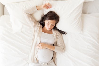 Pregnant woman lies back on pillows in bed