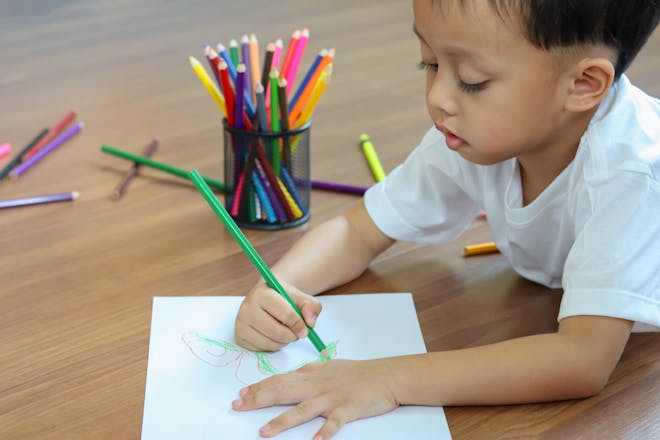 Toddler draws a monster on a sheet of paper next to a pot of coloured pencils