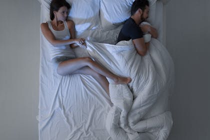 Couple in bed fighting over duvet