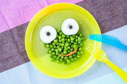 Bowl of peas with cucumber for eyes and a carrot smile so looks like a frog