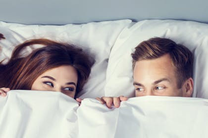 woman and man looking at each other from below a duvet