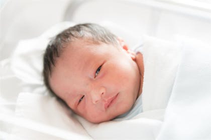 Newborn baby with a full head of hair and eyes opening