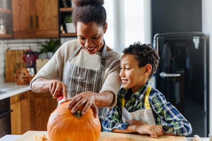 Mother and son carving a pumpkin together in the kitchen