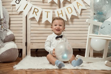 A kid at a party holds a balloon with a birthday banner behind him