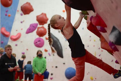 A young girl with a plait wearing a black vest clings to a wall at BoulderWorld Belfast