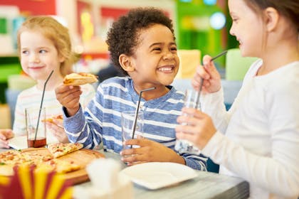 Three children eating pizza and smiling at the dinner table