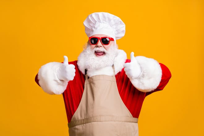 Santa wearing an apron and chef's hat with his thumbs up