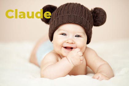 Baby wearing brown wool hat with pom poms for ears. Name Claude written in text