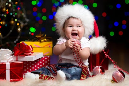 Laughing baby wearing a big fluffy Santa hat and sitting near gifts