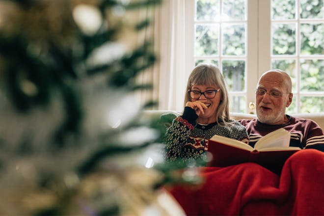 Couple reading and laughing together next to Christmas tree