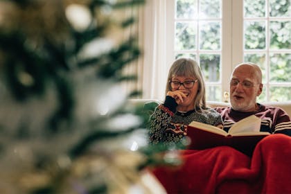 Couple reading and laughing together next to Christmas tree