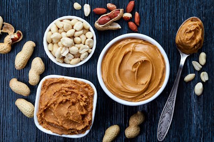 Bowl of peanuts and two bowls of peanut butter surrounded by peanuts in shells