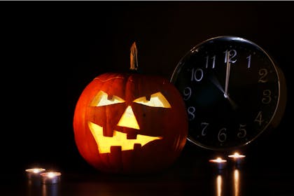 A Halloween pumpkin sits in the dark next to a clock that reads midnight