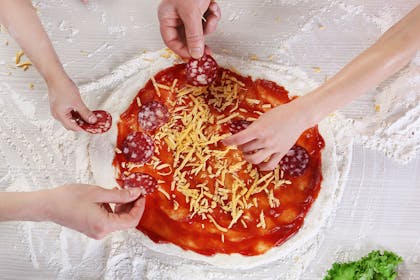 Hands putting different toppings on a pizza