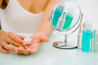 woman holding cream tub with mirror next to her