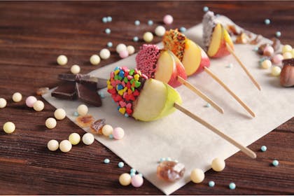 Apple slices coated in chocolate, toffee and cake sprinkles served on lollipop sticks for Halloween