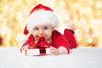 Cute baby wearing Santa outfit and clutching a gift with a red ribbon