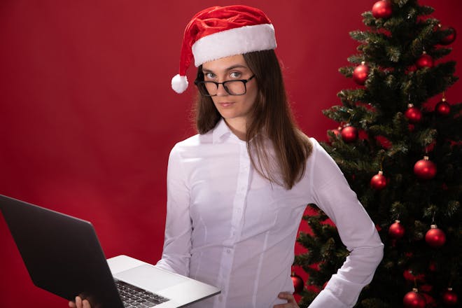Lady wearing Santa hat in front of Christmas tree hlding a laptop