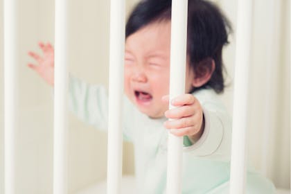 Baby crying holding bars of cot